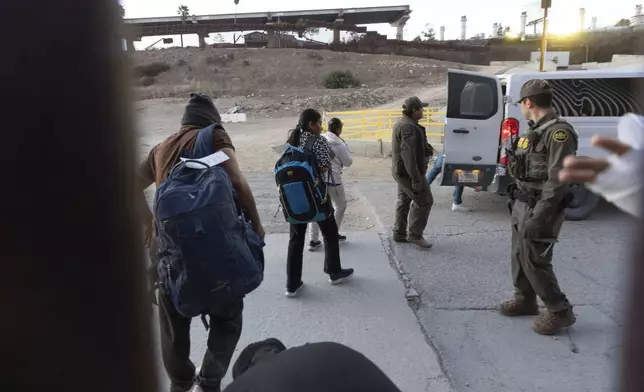 Migrants make their way to a Border Patrol van after crossing illegally and waiting to apply for asylum between two border walls separating Mexico and the United States, Tuesday, Jan. 21, 2025, in San Diego. (AP Photo/Gregory Bull)