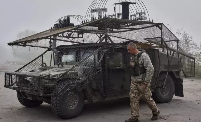 In this photo provided by Ukraine's 65th Mechanized Brigade press service, a Ukrainian soldier passes by an armoured Hummer vehicle equipped with an anti-drone net on the frontline in the Zaporizhzhia region, Ukraine, Monday, May 5, 2025. (Andriy Andriyenko/Ukraine's 65th Mechanized Brigade via AP)
