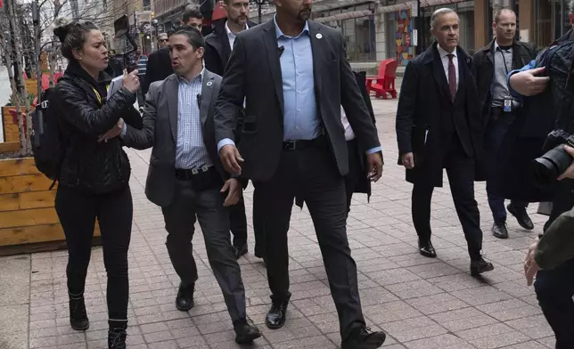 Security keeps a person from the right-wing media group Rebel News away from Prime Minister Mark Carney as he walks to a news conference, in Ottawa, Friday, May 2, 2025. (Adrian Wyld/The Canadian Press via AP)
