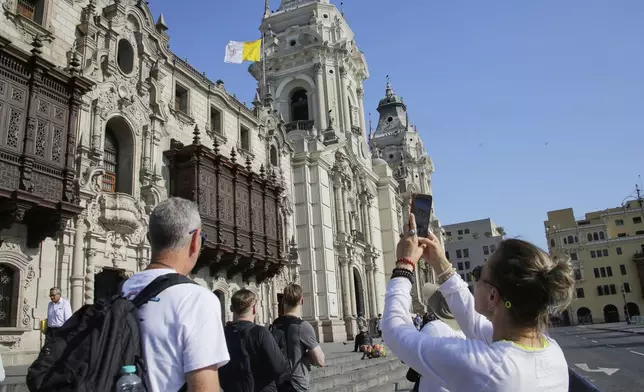A woman photographs the Vatican flag flying above the Cathedral in Lima, Peru, following the election of Robert Prevost, a dual citizen of the United States and Peru who served as a missionary and bishop in the country, as Pope Leo XIV, Thursday, May 8, 2025. (AP Photo/Cesar Zamalloa)