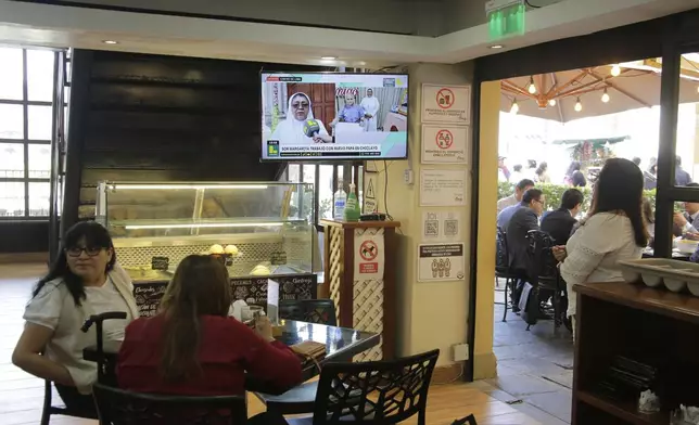 Diners lunch in a restaurant where a television programs airs an interview with a nun who used to work alongside Robert Prevost, who was elected as the new pope, taking the name Leo XIV, in Lima, Peru, Thursday, May 8, 2025. (AP Photo/Cesar Zamalloa)