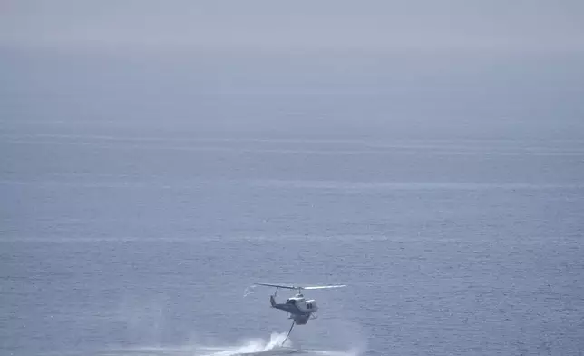 A helicopter fills water from the sea during the "Through Fire 2025" drill in Lavrio, about 60 kilometres (37 miles) southeast of Athens, Greece, Thursday, May 22, 2025. (AP Photo/Thanassis Stavrakis)