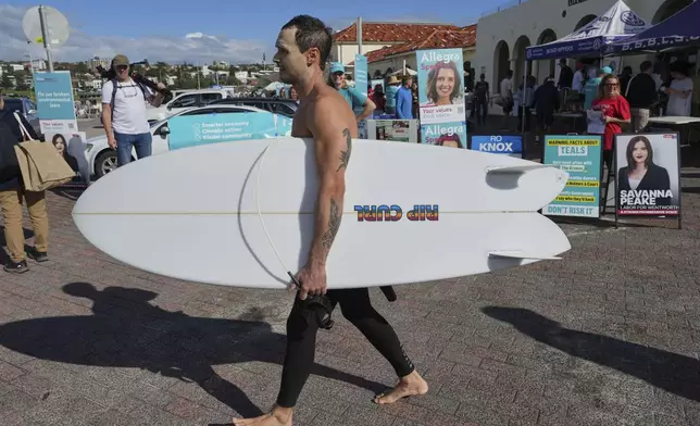A surfer carries his board as he walks past a polling booth at Sydney's Bondi Beach, Saturday, May 3, 2025. (AP Photo/Mark Baker)