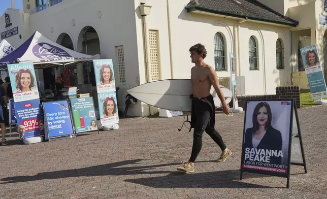 A surfer carries his board as he walks past a polling booth at Sydney's Bondi Beach, Saturday, May 3, 2025. (AP Photo/Mark Baker)