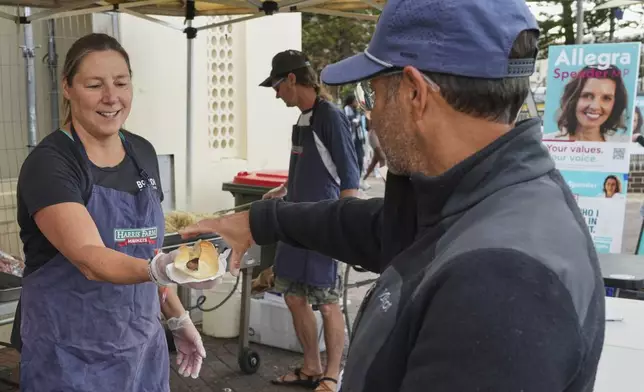A volunteer hands a customer a sausage in a bread roll outside a polling booth at Sydney's Bondi Beach, Saturday, May 3, 2025. (AP Photo/Mark Baker)
