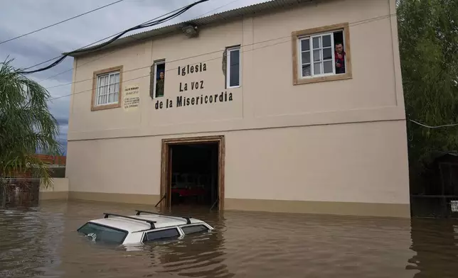 A vehicle sits partially submerged in floodwaters as residents look out from the windows of a church, following heavy rains in Campana, Argentina, Saturday, May 17, 2025. (AP Photo/Rodrigo Abd)