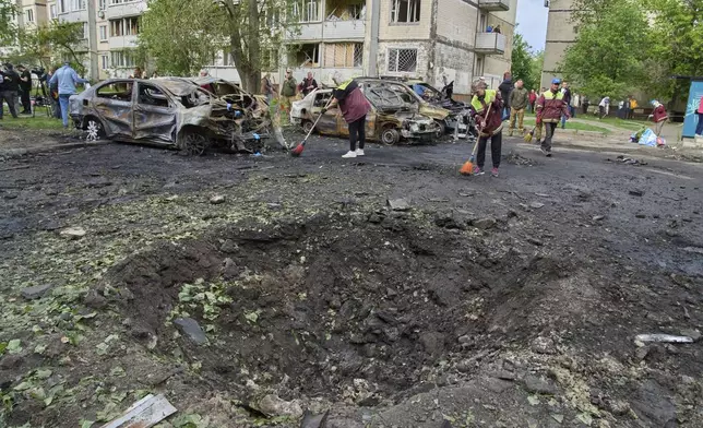 Municipal workers clean up near burnt cars and a crater made by a drone in the residential area following Russia's air raid in Kyiv, Ukraine, Sunday, May 4, 2025. (AP Photo/Efrem Lukatsky)