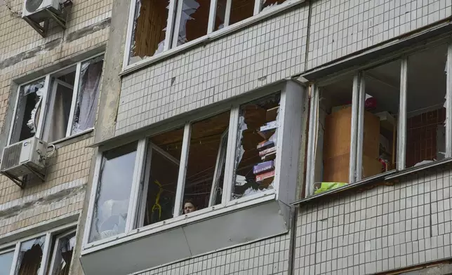 A resident looks out of the broken window in an apartment house following Russia's drone attack in Kyiv, Ukraine, Sunday, May 4, 2025. (AP Photo/Efrem Lukatsky)