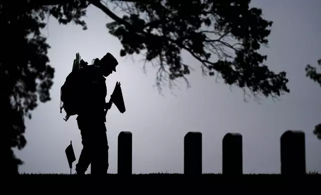 A member of the 3rd U.S. Infantry Regiment places flags at the headstones of service members buried at Arlington National Cemetery, ahead of Memorial Day, Thursday, May 22, 2025, in Arlington, Va. (AP Photo/Julia Demaree Nikhinson)