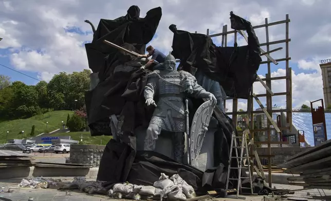 Municipal workers remove the cover that protected a monument of Kyiv legendary founders from Russian missile attacks on the fourth year of Russia-Ukraine war on the country's main square in Kyiv, Ukraine, Wednesday, May 21, 2025. (AP Photo/Efrem Lukatsky)(