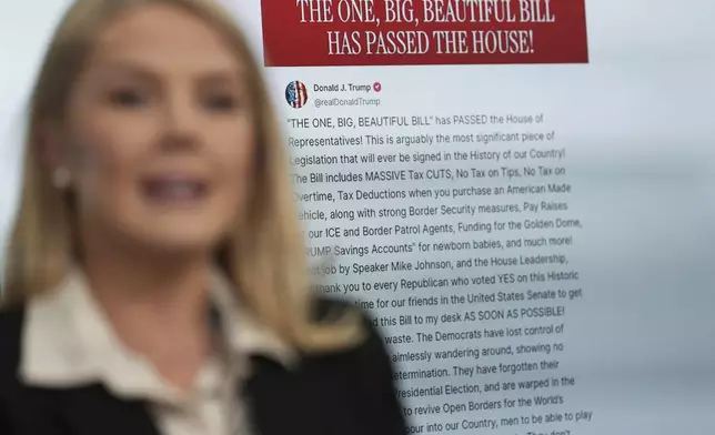 White House press secretary Karoline Leavitt speaks with reporters as an image of President Donald Trump's post on Truth Social regarding the tax cuts package appears on screen in the James Brady Press Briefing Room at the White House, Thursday, May 22, 2025, in Washington. (AP Photo/Jacquelyn Martin)