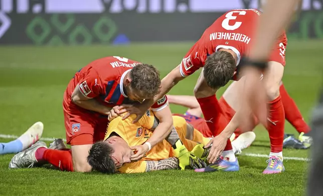 Heidenheim's Tim Siersleben, left, and Jan Schöppner provide first aid to goalkeeper Kevin Müller following an injury during the Bundesliga soccer match between FC Heidenheim and VfL Bochum at Voith-Arena. Heidenheim, Germany, Friday May 2, 2025. (Harry Langer/dpa via AP)