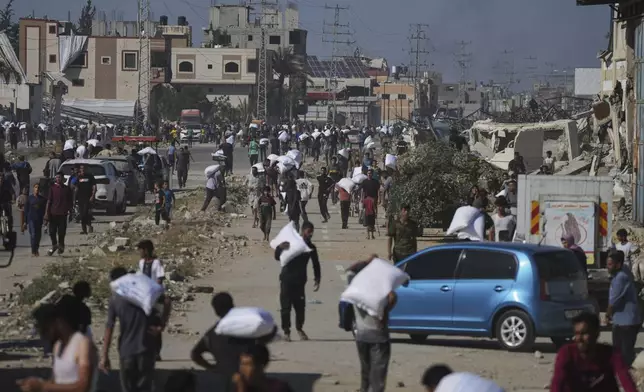 Palestinians carry bags of flour after storming a U.N. World Food Program warehouse in Zawaida, Central Gaza Strip, on Wednesday, May 28, 2025. (AP Photo/Abdel Kareem Hana)