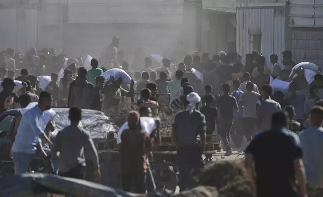 Palestinians carry bags of flour after storming a U.N. World Food Program warehouse in Zawaida, Central Gaza Strip, on Wednesday, May 28, 2025. (AP Photo/Abdel Kareem Hana)