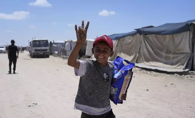 A Palestinian child smiles to the camera as carries a bag of rice delivered by the U.S.-backed Gaza Humanitarian Foundation, after receiving the supplies in Rafah, as he arrive in Khan Younis, southern Gaza Strip, on Wednesday, May 28, 2025. (AP Photo/Abdel Kareem Hana)