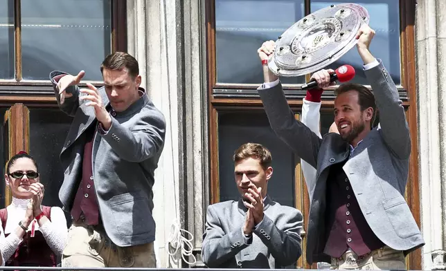 Bayern's Harry Kane, right, stands with the championship trophy next to his teammates goalkeeper Manuel Neuer, 2nd left, and Joshua Kimmich, center, on the town hall balcony, at the championship celebration in Munich, Germany, Sunday, May 18, 2025. (Daniel Loeb/dpa via AP)