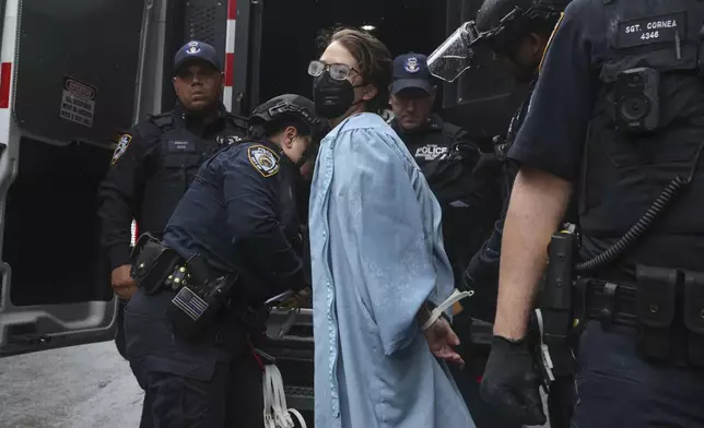 A person wearing graduate robes is detained by police across the street from the main gates of Columbia University, Wednesday, May 21, 2025, in New York. (AP Photo/Heather Khalifa)