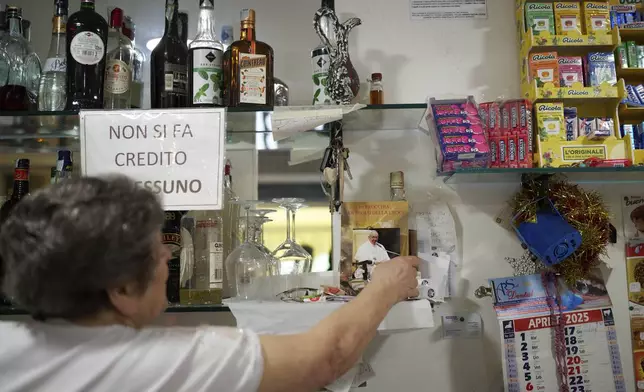 A woman adjusts a photo of the late Pope Francis in cafe in front of San Paolo Della Croce parish church in Corviale neighbourhood, in Rome, Sunday, May 4, 2025. (AP Photo/Alessandra Tarantino)