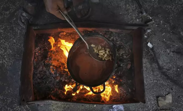 A Palestinian mother cooks beans over a fire fueled by burning plastic at a tent sheltering displaced families in Gaza City, Saturday, May 24, 2025. (AP Photo/Jehad Alshrafi)