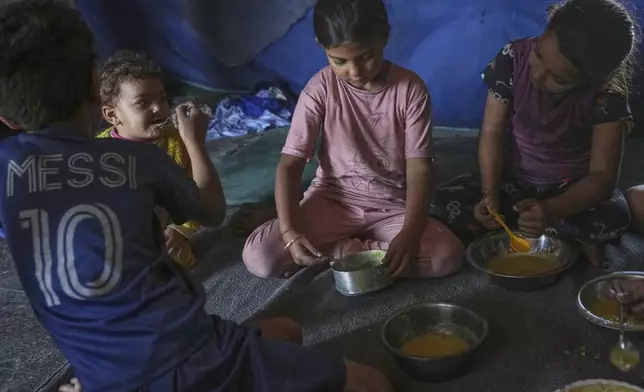 Children from the Saqr family eat lentil soup cooked by their mother at their family tent in Gaza City, Saturday, May 24, 2025. (AP Photo/Jehad Alshrafi)
