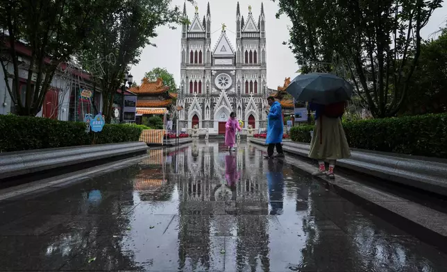 Visitors with rain gears take pictures as they visiting the Xishiku Catholic Church during a rainy day, in Beijing, Friday, May 9, 2025. (AP Photo/Andy Wong)