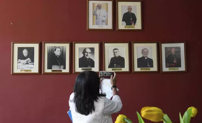 A woman takes photos of a photos of portraits of former bishops of Callao, including a portrait of Pope Leo XIV, far right, from when he was the Apostolic administrator in 2020, at the Diocese office in Callao, Peru, Friday, May 9, 2025. (AP Photo/Martin Mejia)