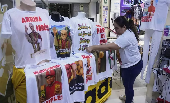 Vicky Quinones displays T-shirts featuring images of newly elected Pope Leo XIV and references to his time in Peru at a printing shop in Lima, Friday, May 9, 2025. (AP Photo/Martin Mejia)