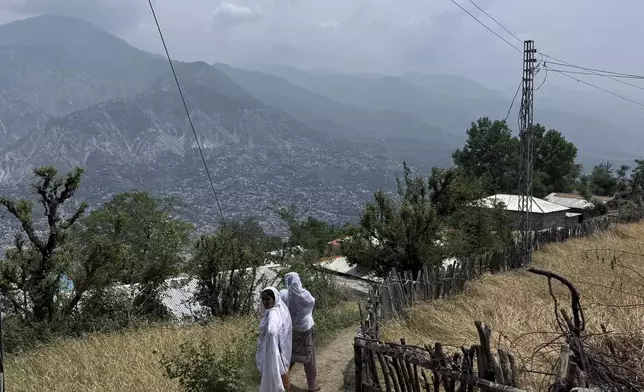 Villager women walk on a dusty track during a government's organized trip for media to Bella Noor Shah, a mountainous village near Muzaffarabad, the capital of Pakistan administered Kashmir, Monday, May 5, 2025. (AP Photo/Muhammad Yousuf, Pool)