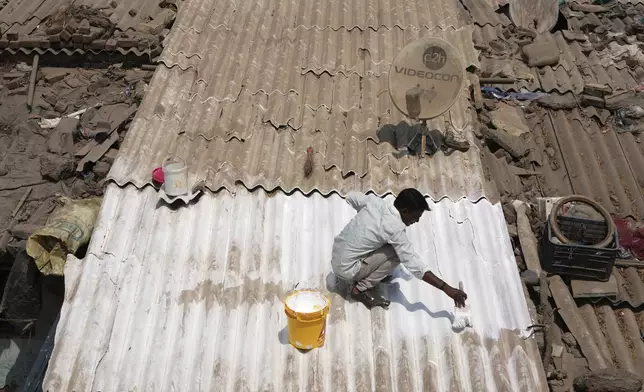 A man applies reflective paint to the roof of a house that helps keep the indoors cooler in Ahmedabad, India, Wednesday, April 2, 2025. (AP Photo/Ajit Solanki)