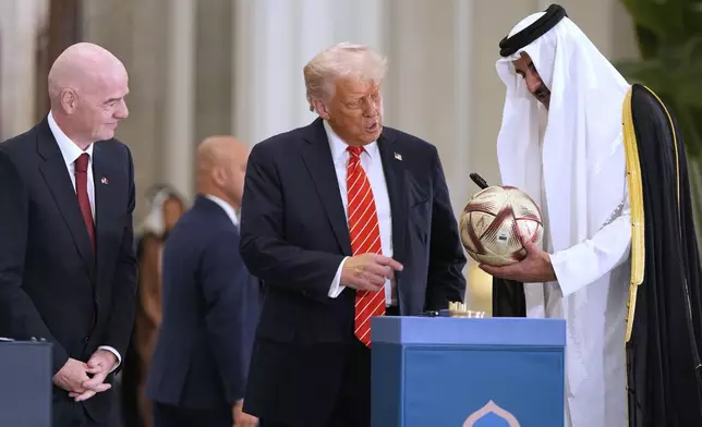 Qatar's Emir Sheikh Tamim bin Hamad Al Thani signs a FIFA soccer ball as President Donald Trump and FIFA President Gianni Infantino look on, at the Lusail Palace, Wednesday, May 14, 2025, in Doha, Qatar, as they marked the passing of World Cup hosting duties from Qatar, which held it in 2022, to the United States, which is hosting in 2026. (AP Photo/Alex Brandon)