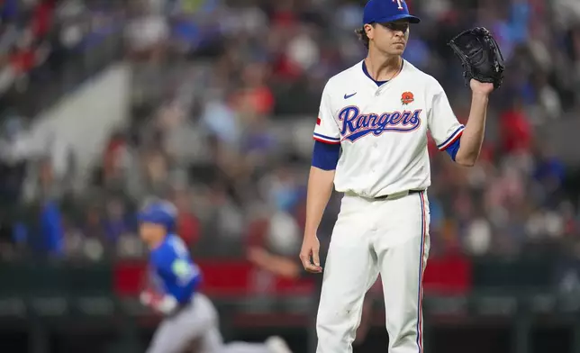 Texas Rangers starting pitcher Jacob deGrom, right, waits for a new ball as Toronto Blue Jays' Daulton Varsho, left, runs the bases after hitting a solo home run during the first inning of a baseball game, Monday, May 26, 2025, in Arlington, Texas. (AP Photo/Julio Cortez)
