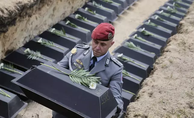 with the remains of fallen German soldiers of WWII to the grave during a funeral service at a memorial site for fallen soldiers in Halbe, Germany, Wednesday, April 30, 2025. (AP Photo/Ebrahim Noroozi)