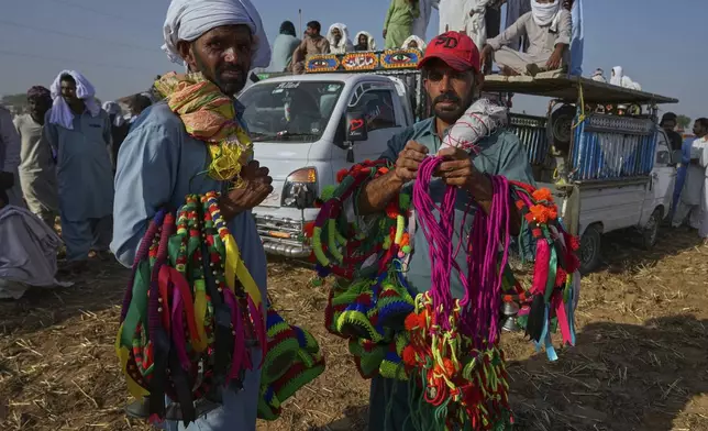 Hawkers hold colourful ribbons and other items using to decorate bull as they wait for customers at the venue of a traditional bull race competition, in Malal, a village of Attock district, in Pakistan, Thursday, May 15, 2025. (AP Photo/Anjum Naveed)