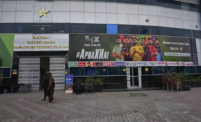 Workers walk past an advertisement board of Pakistan Super League Twenty20 tournament with the pictures of cricketers, installed at the Rawalpindi Cricket Stadium, in Rawalpindi, Pakistan, Friday, May 9, 2025. (AP Photo/Anjum Naveed)