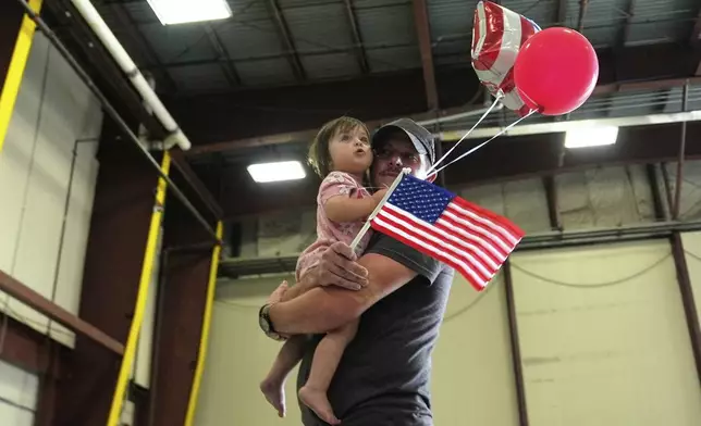 An Afrikaner refugee from South Africa carries a baby with balloons and an American flag as they arrive, Monday, May 12, 2025, at Dulles International Airport in Dulles, Va. (AP Photo/Julia Demaree Nikhinson)