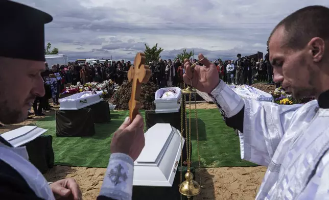 Priests conduct a memorial service for Roman Martyniuk, 17, Tamara Martyniuk, 8, and Stanislav Martyniuk, 12, killed in a Russian strike on Sunday, during farewell ceremony in Korostyshiv, Zhytomyr region, Ukraine, Wednesday, May 28, 2025. (AP Photo/Evgeniy Maloletka)