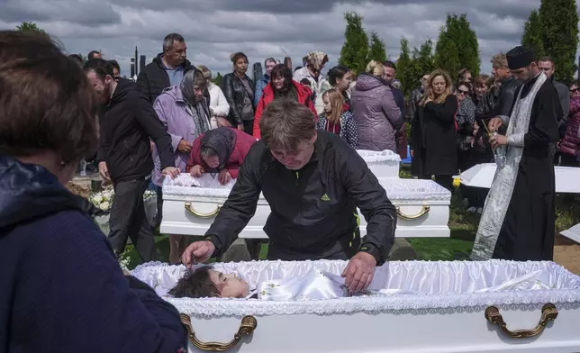 A father mourns his children Roman Martyniuk, 17, Tamara Martyniuk, 8, and Stanislav Martyniuk, 12, killed in a Russian strike on Sunday, during farewell ceremony in Korostyshiv, Zhytomyr region, Ukraine, Wednesday, May 28, 2025. (AP Photo/Evgeniy Maloletka)