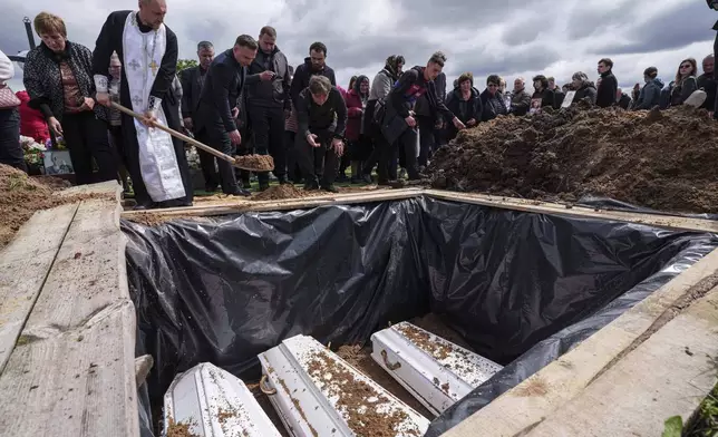 People throw earth into the grave during a funeral ceremony for Tamara Martyniuk, 8, Stanislav Martyniuk, 12, and Roman Martyniuk, 17, killed in a Russian strike on Sunday, in Korostyshiv, Zhytomyr region, Ukraine, Wednesday, May 28, 2025. (AP Photo/Evgeniy Maloletka)