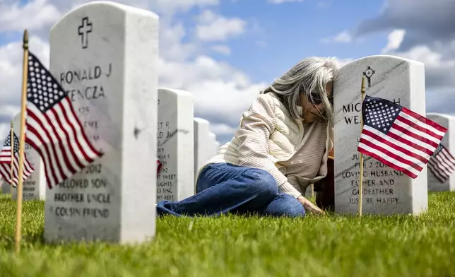 Rosie Weaver leans against the headstone of her husband U.S. Army Spc. Michael Weaver after a Memorial Day ceremony on Sunday, May 25, 2025, at Great Lakes National Cemetery in Holly Township, Mich. Her husband passed in 2011 due to lasting effects of Agent Orange. (Ayrton Breckenridge/The Flint Journal via AP)