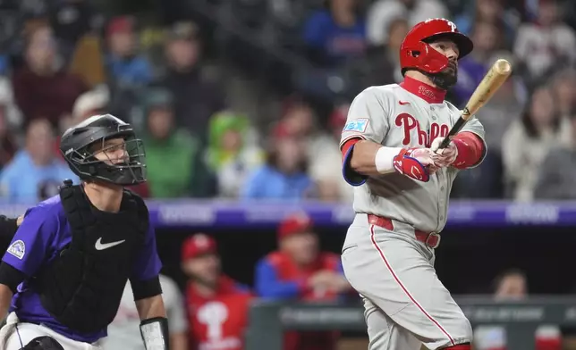 Philadelphia Phillies' Kyle Schwarber, right, follows the flight of his solo home run with Colorado Rockies catcher Jacob Stallings, left, in the ninth inning of a baseball game Monday, May 19, 2025, in Denver. (AP Photo/David Zalubowski)