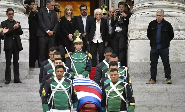 Uruguay's President Yamandu Orsi, back left, his wife Laura Alonsoperez, second from left, and Lucia Topolansky, the widow of late former President Jose Mujica, watch the honor guard carry his casket after funeral ceremonies at the Legislative Palace in Montevideo, Uruguay, Thursday, May 15, 2025. (AP Photo/Santiago Mazzarovich)