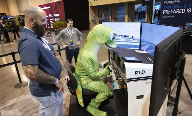 Sean DeFendi of Virginia Beach, left, watches over the GEICO Gecko as he uses the Flight Safety International flight simulator in CHI Health Center Omaha for the Berkshire Hathaway annual meeting Saturday, May 3, 2025, in Omaha, Neb. (AP Photo/Rebecca S. Gratz)