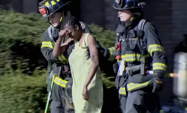 This image taken from video provided by WISN show a resident being escorted by firefighters at the site of an apartment building fire in Milwaukee, Wis., Sunday, May 11, 2025. (WISN via AP)