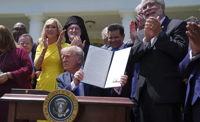 President Donald Trump, surrounded by religious leaders, holds up a signed executive order establishing the Religious Liberty Commission, during a National Day of Prayer event in the Rose Garden of the White House, Thursday, May 1, 2025, in Washington. (AP Photo/Evan Vucci)