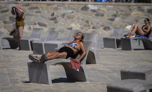 FILE - People sunbathe on a promenade in Barcelona, Spain, Wednesday, July 24, 2024. Several regions of Spain are under alert for high temperatures. (AP Photo/Emilio Morenatti,File)