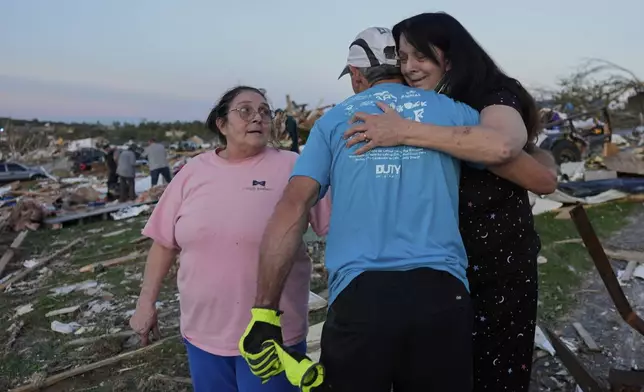 Bea Johnson, left, looks to her sister Kristie Sexton, right, as she is embraced by family friend Keith Adams as they stand next to Sexton's destroyed home after a severe storm passed through the area, Saturday, May 17, 2025, in London, Ky. (AP Photo/Carolyn Kaster)