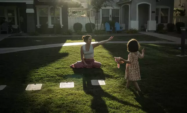 Maria Padron, center, plays with her daughter Fae Padron, 4, right, in a "kid pod," a cluster of families with more than 20 kids between them, at Agritopia, a community nestled around a plot of agricultural land, April 21, 2025, in Gilbert, Ariz. (AP Photo/Annika Hammerschlag)