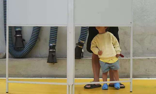 A child watches a voter fill their ballot in Portugal's general election at polling station in Lisbon, Sunday, May 18, 2025. (AP Photo/Ana Brigida)