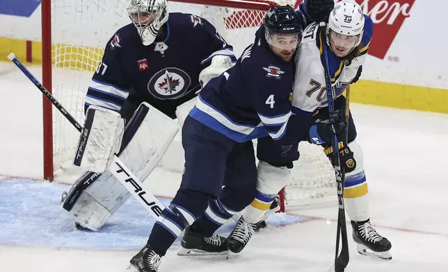 Winnipeg Jets' Neal Pionk (4) defends against St. Louis Blues' Oskar Sundqvist (70) in front of goaltender Connor Hellebuyck (37) during the third period of an NHL playoff game in Winnipeg on Wednesday, April 30, 2025. (John Woods/The Canadian Press via AP)