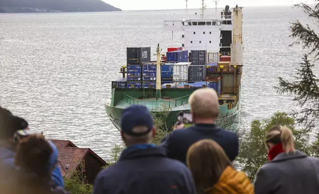 People observe a 135-meter-long container ship that ran aground in the Trondheimsfjord, outside Byneset, in Trondheim, Norway, Thursday May 22, 2025. The container ended up on land near a house on Thursday night. (Jan Langhaug/NTB Scanpix via AP)